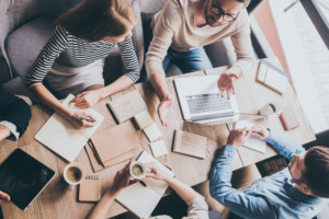 Seen from above, a team sits at the office table at a joint meeting and discusses