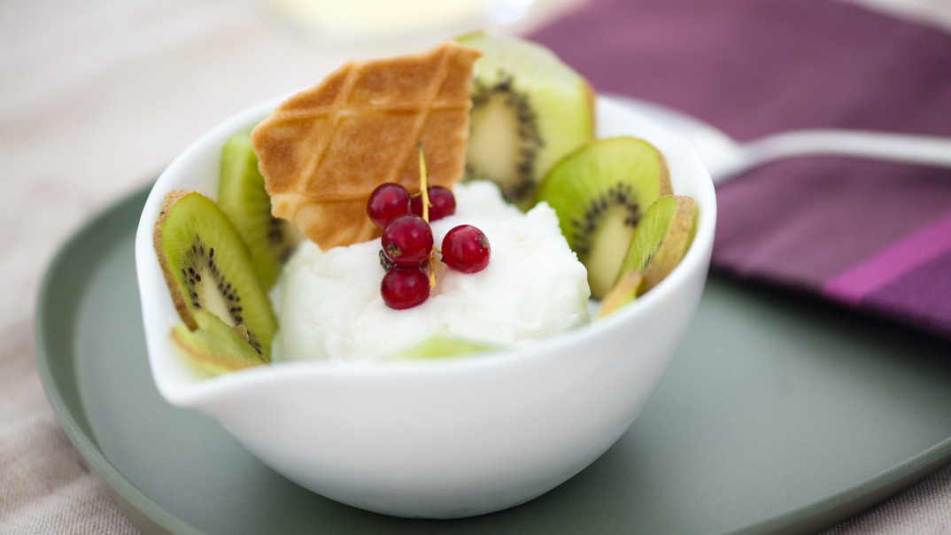 Eiscreme mit Kiwi-Scheiben und Wafflen garniert in einer Schuessel angerichtet