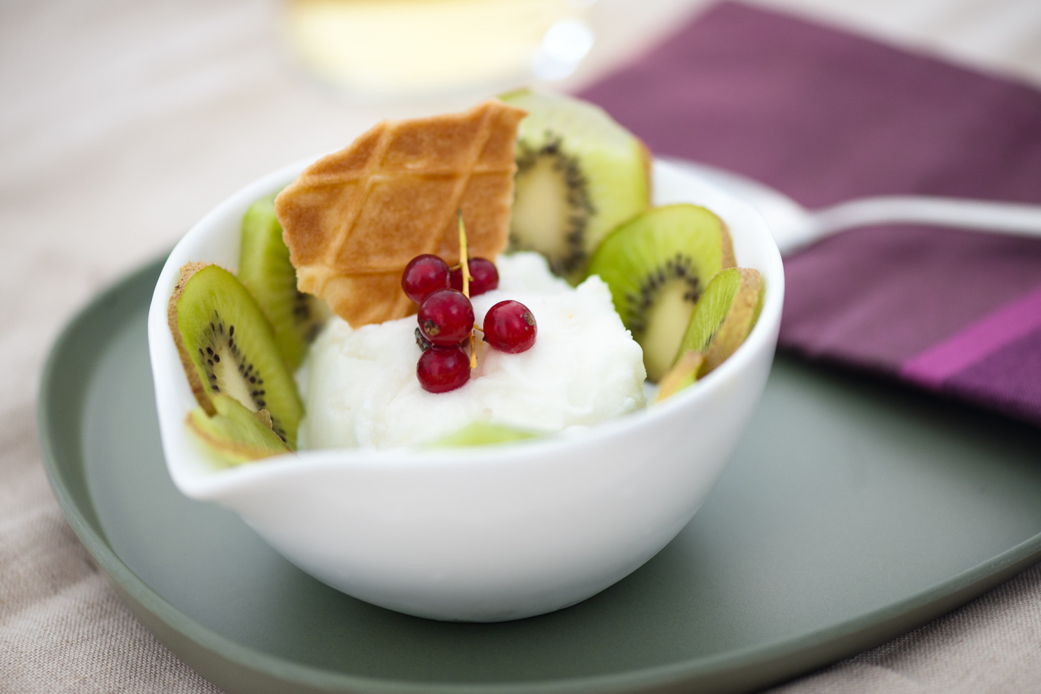 Eiscreme mit Kiwi-Scheiben und Wafflen garniert in einer Schuessel angerichtet