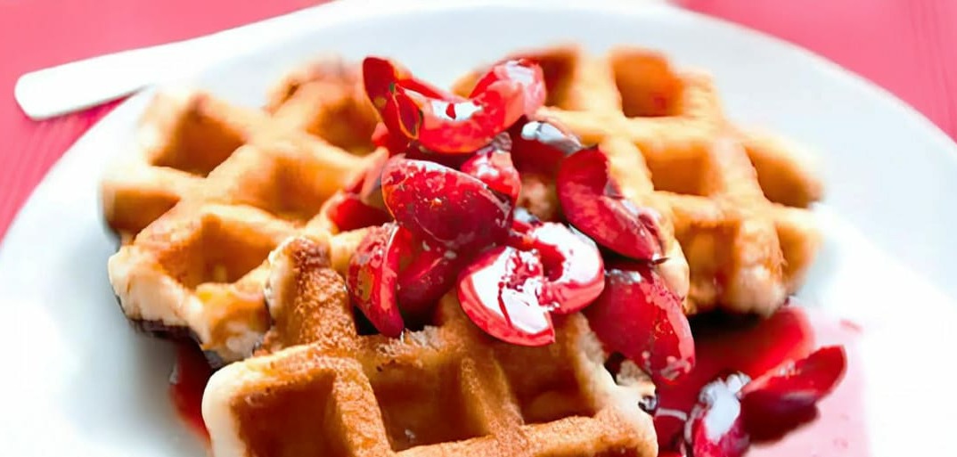 Sweet waffles with warm cherries and cream – a delicious and fruity dessert or breakfast treat