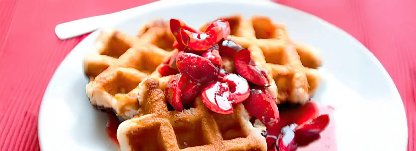 Sweet waffles with warm cherries and cream – a delicious and fruity dessert or breakfast treat