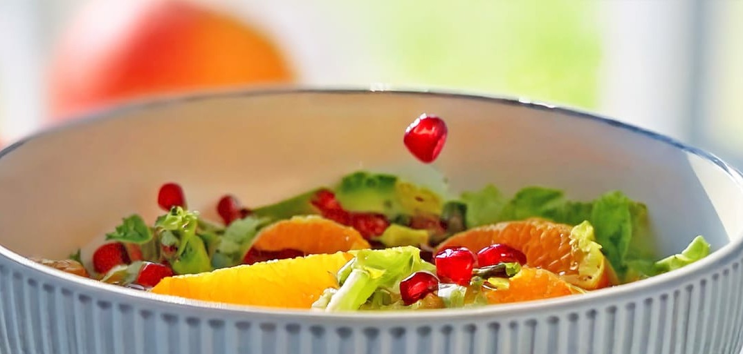 Fresh citrus salad with pomegranate seeds and avocado, lettuce on a white plate – a vibrant, healthy dish.