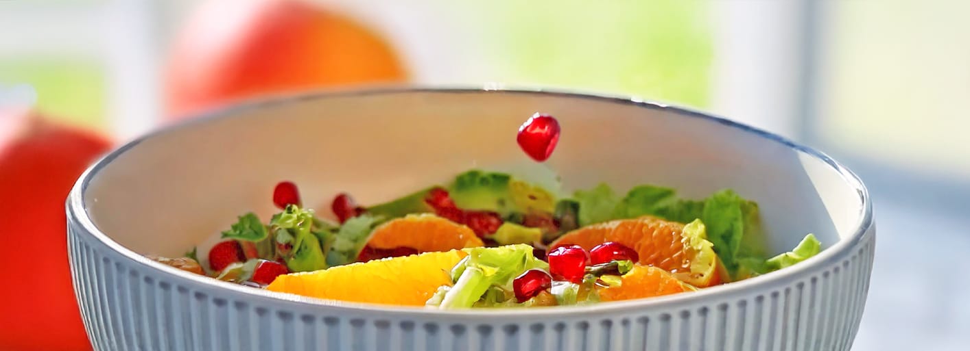 Fresh citrus salad with pomegranate seeds and avocado, lettuce on a white plate – a vibrant, healthy dish.