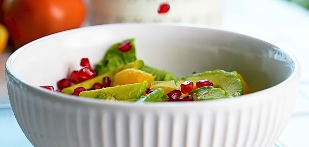 Fresh citrus salad with pomegranate seeds and avocado, garnished with mint on a white plate – a vibrant, healthy dish.