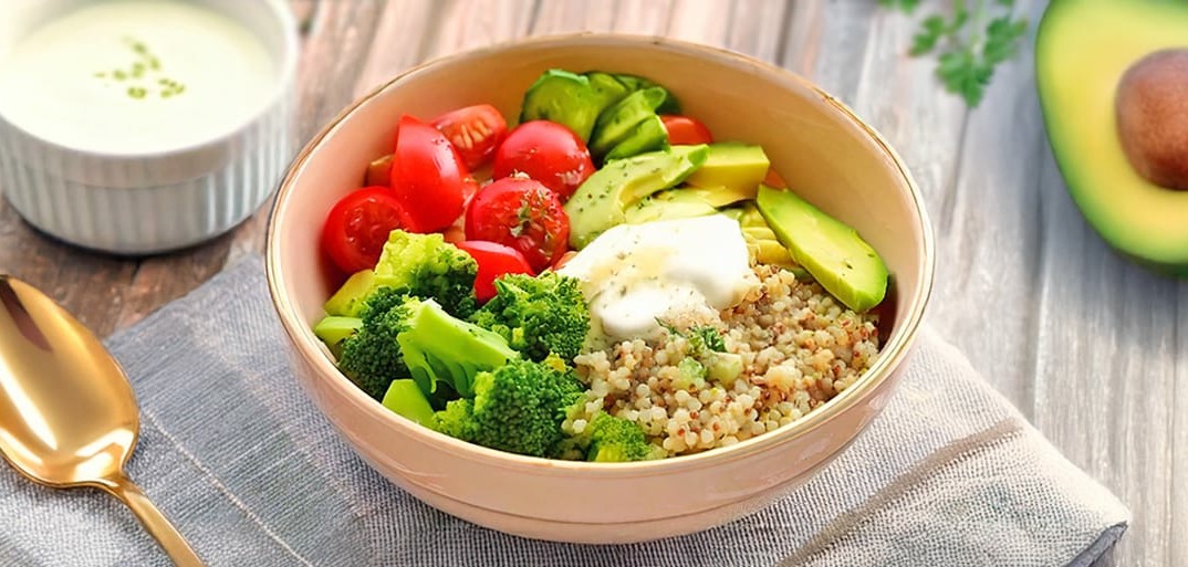 Colorful quinoa bowl with avocado, cherry tomatoes, cucumber, sweet potato, and Tzatziki, served fresh and healthy