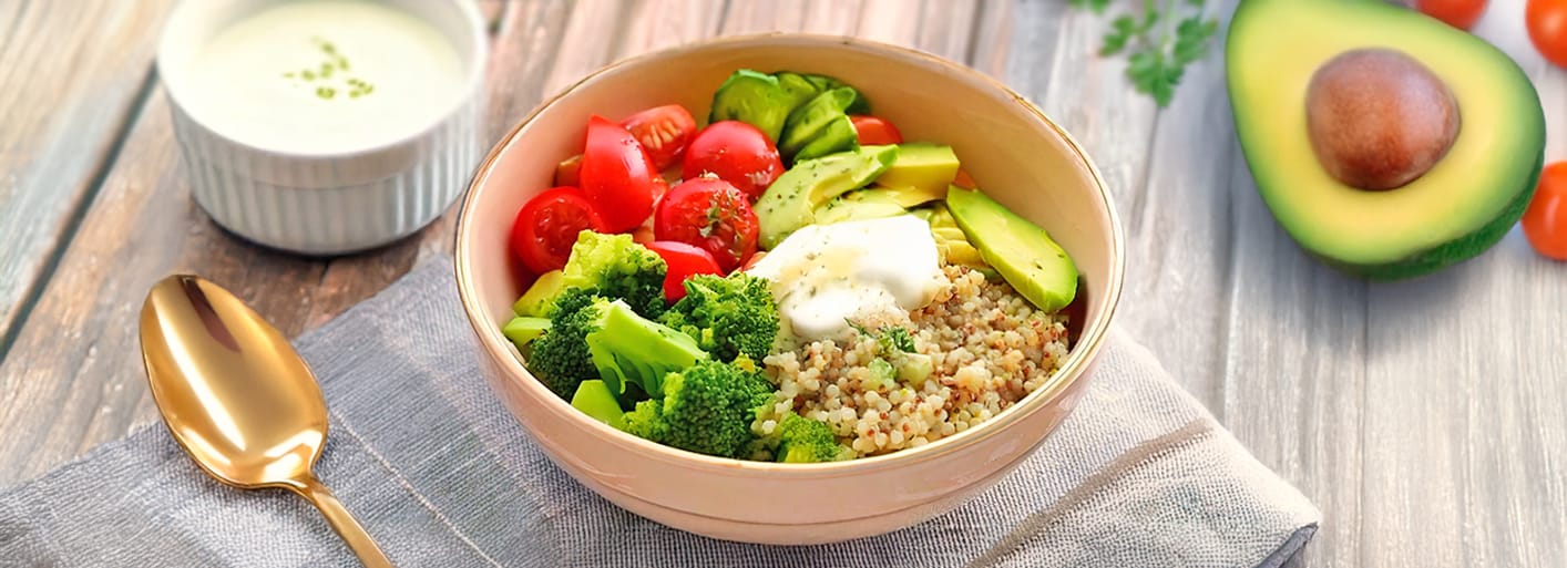 Colorful quinoa bowl with avocado, cherry tomatoes, cucumber, sweet potato, and Tzatziki, served fresh and healthy