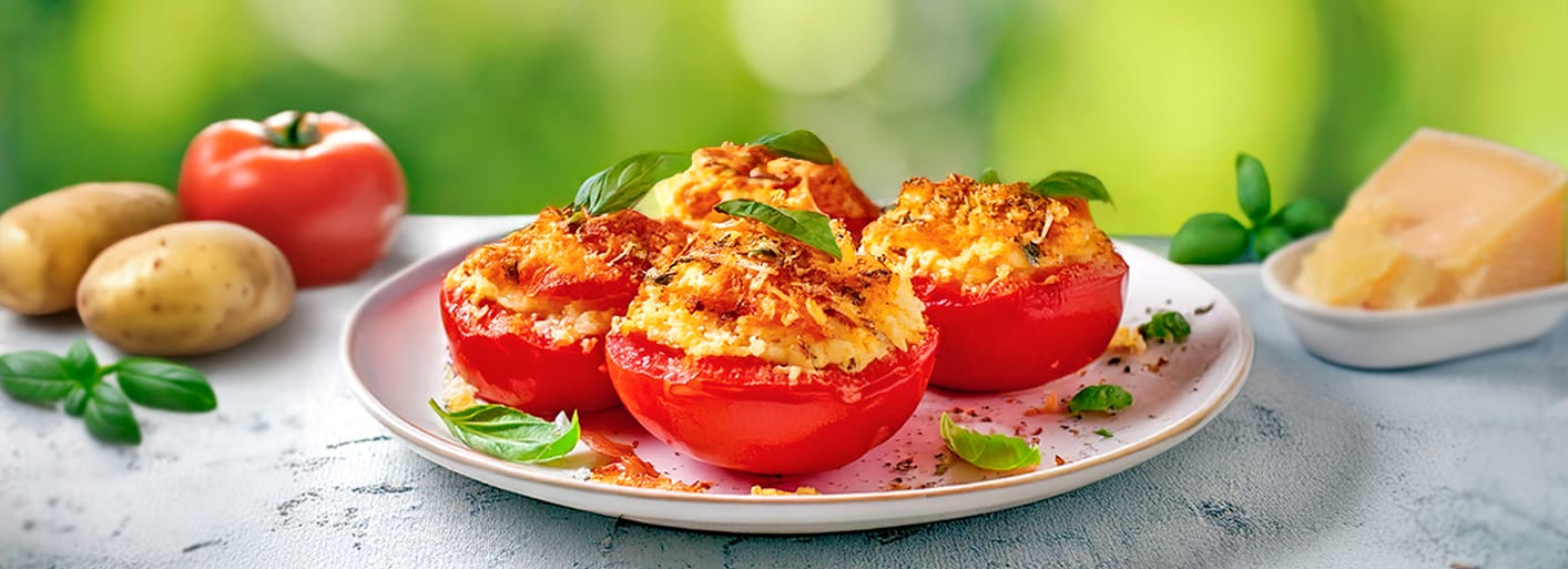 A plate of stuffed tomatoes topped with cheese, garnished with fresh basil leaves.